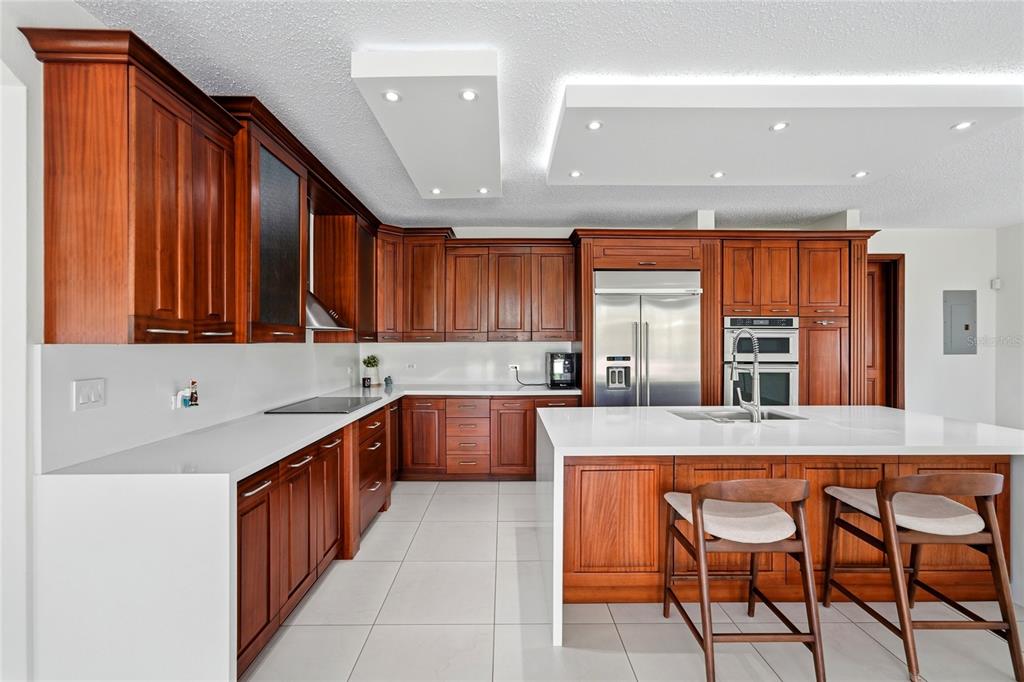 A modern kitchen features cherry wood cabinets, white countertops, a large island, and recessed lighting — Bloque LN SOLAR 27, CAGUAS, PR