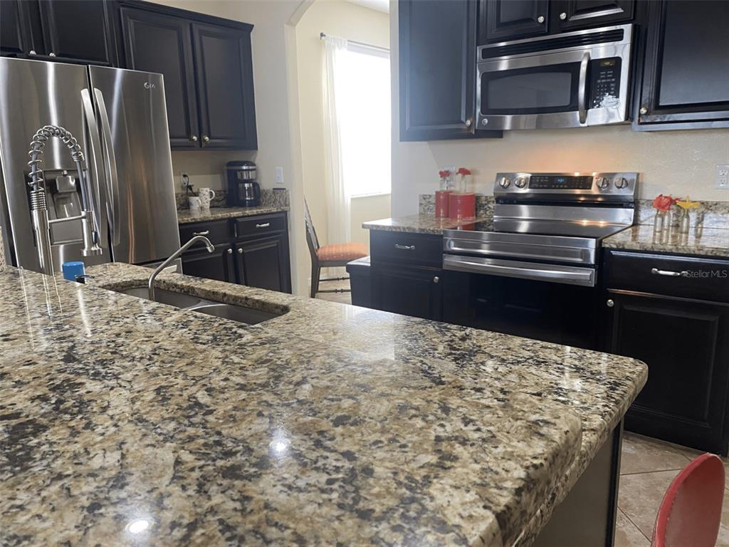 A kitchen features dark wood cabinets, granite countertops, and stainless steel appliances — 408 19TH STREET NW, RUSKIN, FL