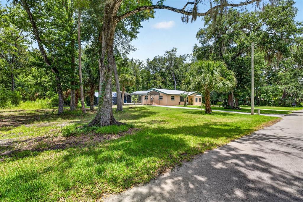A single-story house with a carport sits on a grassy lot surrounded by trees — 5304 S JAMES TERRACE, HOMOSASSA, FL