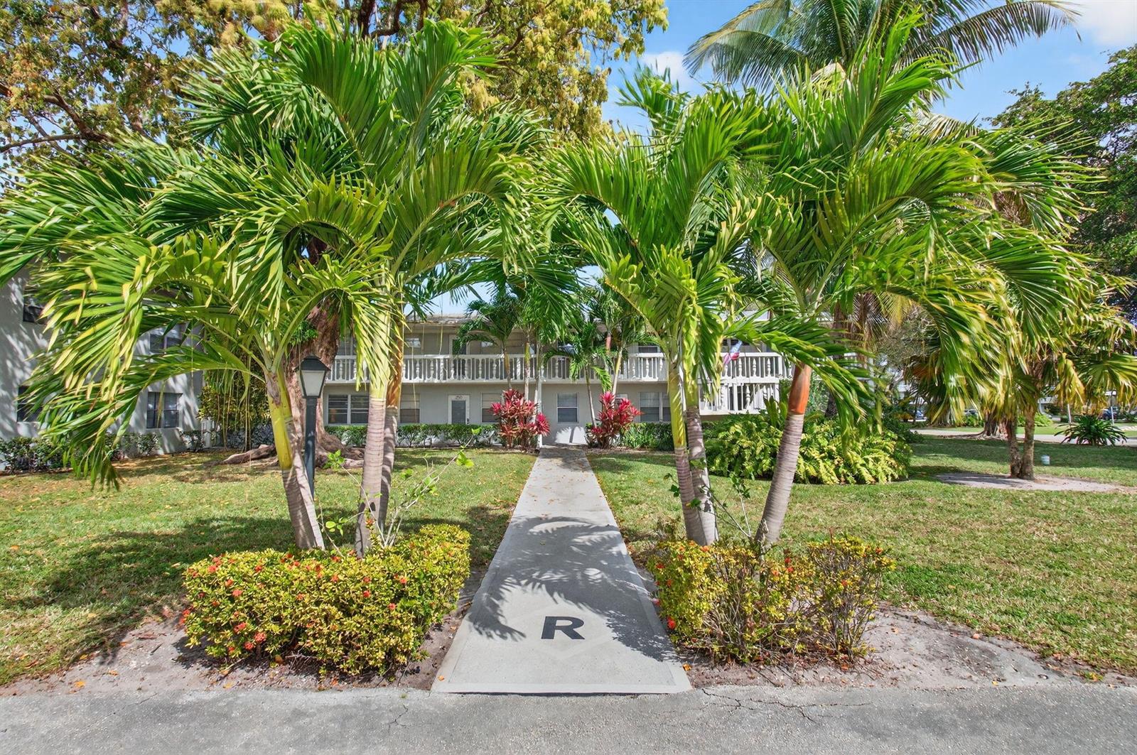 A concrete walkway with a letter R leads to a two-story apartment building with palm trees — 247 Ventnor R, Deerfield Beach FL 33442, DEERFIELD BEACH, FL