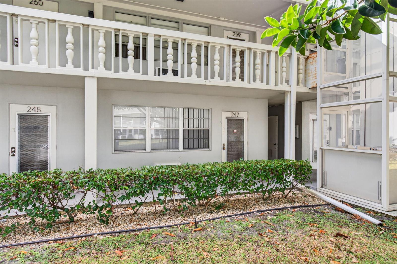 The exterior of a two-story apartment building features a white balcony railing and green hedges — 247 Ventnor R, Deerfield Beach FL 33442, DEERFIELD BEACH, FL