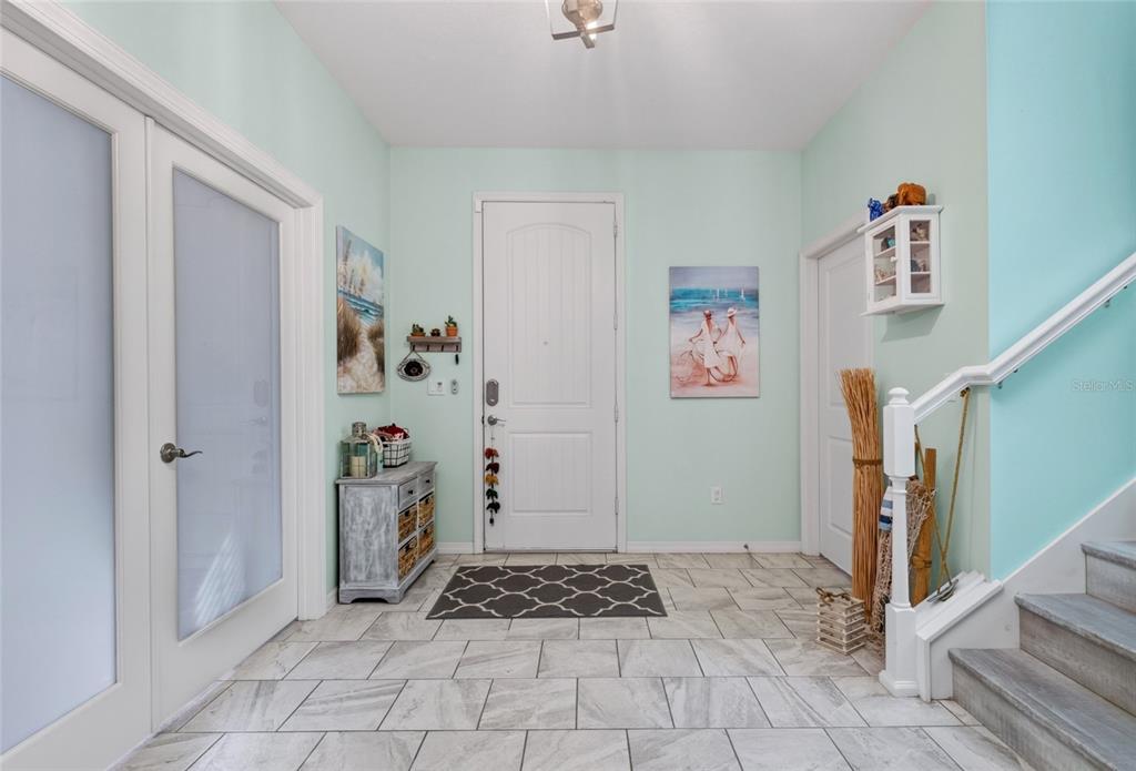 A light-colored entryway features a white front door, tiled flooring, a staircase, and coastal decor — 14735 SNOWY EGRET STREET, WINTER GARDEN, FL