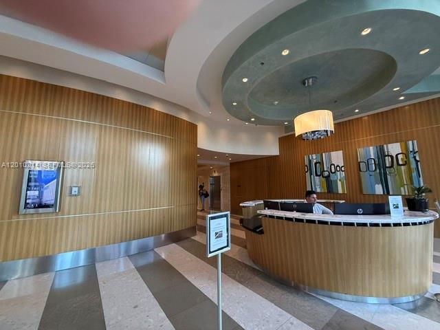 A modern lobby features a curved wooden reception desk, a circular ceiling detail, and artwork — 175 SW 7th St # 1605, Miami FL 33130, MIAMI, FL