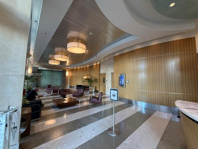A modern building lobby features a wood-paneled wall, marble floors, and circular pendant lighting — 175 SW 7th St # 1605, Miami FL 33130, MIAMI, FL
