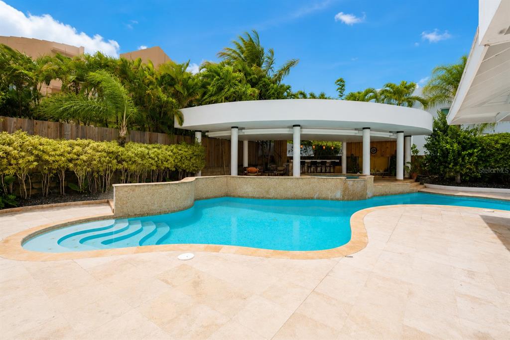 A swimming pool with a curved stone wall sits in front of a covered patio — 16 CALLE PALMA DE COCO, DORADO, PR