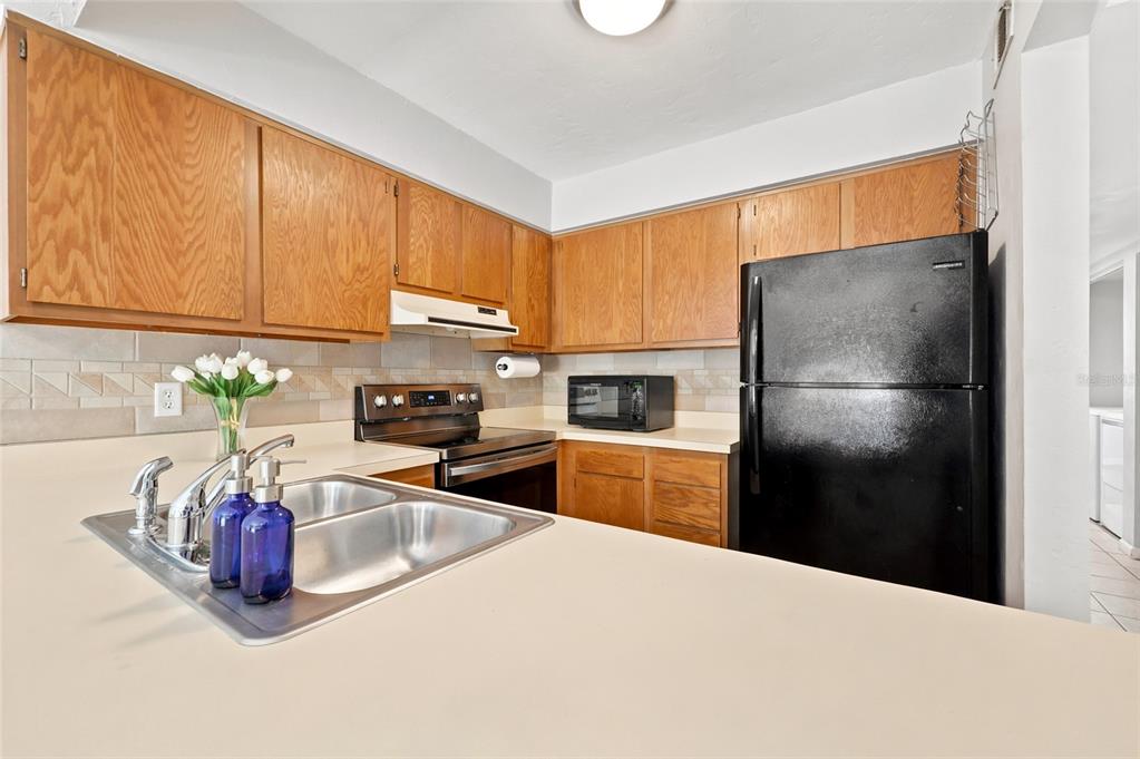 A kitchen features oak cabinets, a black refrigerator, a stainless steel stove, and a sink — 4431 SW 21ST LANE, GAINESVILLE, FL