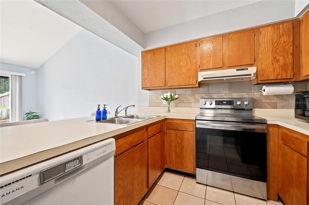 A kitchen features wood cabinets, a stainless steel stove, a dishwasher, and a tiled backsplash — 4431 SW 21ST LANE, GAINESVILLE, FL