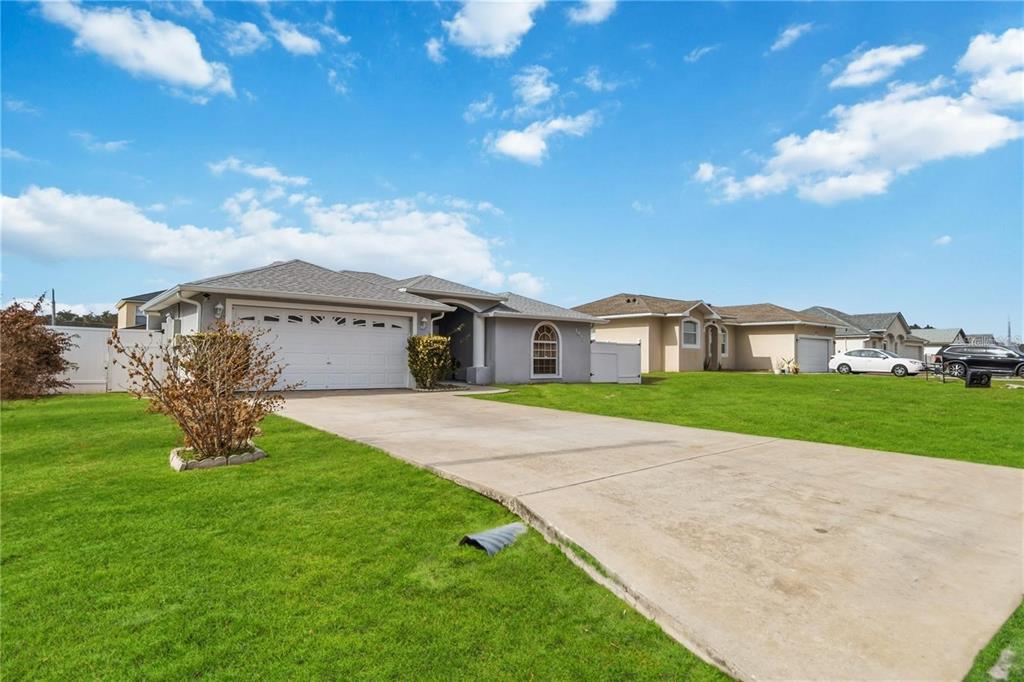 A single-story suburban house with a concrete driveway, two-car garage, and a green lawn — 1912 MANATEE DR, POINCIANA, FL