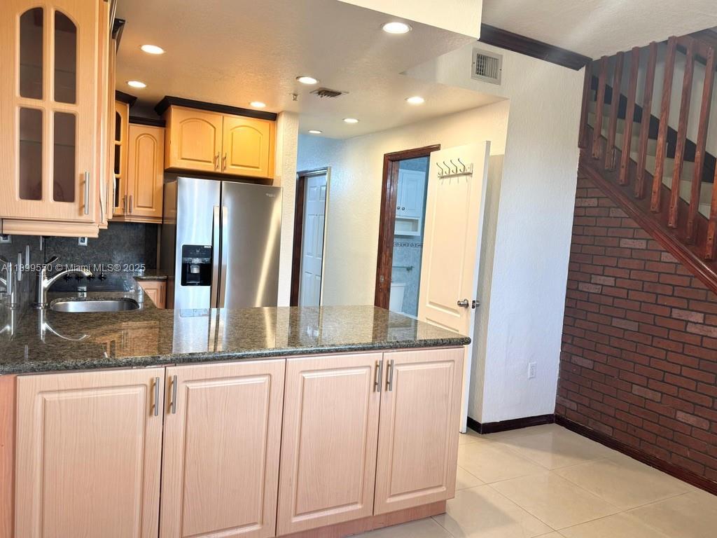 A kitchen features light wood cabinets, granite countertops, a stainless steel refrigerator, and brick stairs — 420 E 1st Ave # B204, Hialeah FL 33010, HIALEAH, FL