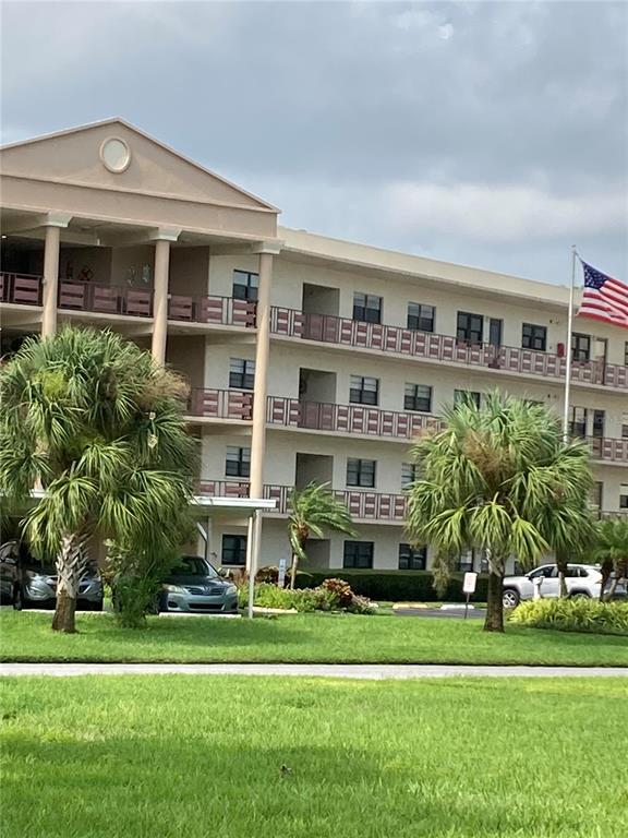 A multi-story apartment building with balconies and palm trees sits behind a grassy lawn — 7975 58TH AVENUE N UNIT 408, ST PETERSBURG, FL