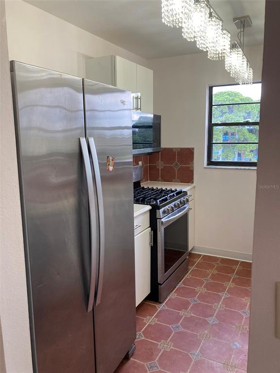 A kitchen features stainless steel appliances, white cabinetry, and reddish-brown tiled flooring — 7975 58TH AVENUE N UNIT 408, ST PETERSBURG, FL