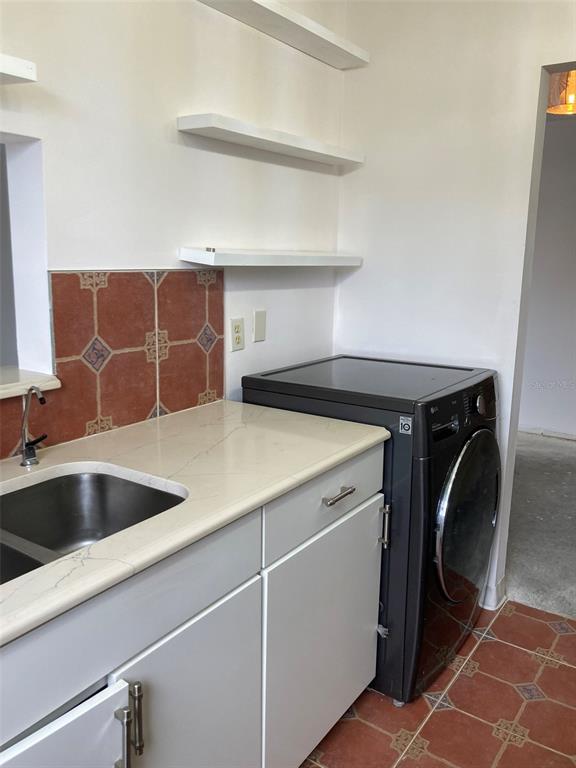 A kitchen area features a stainless steel sink, white cabinets, floating shelves, and a washing machine — 7975 58TH AVENUE N UNIT 408, ST PETERSBURG, FL