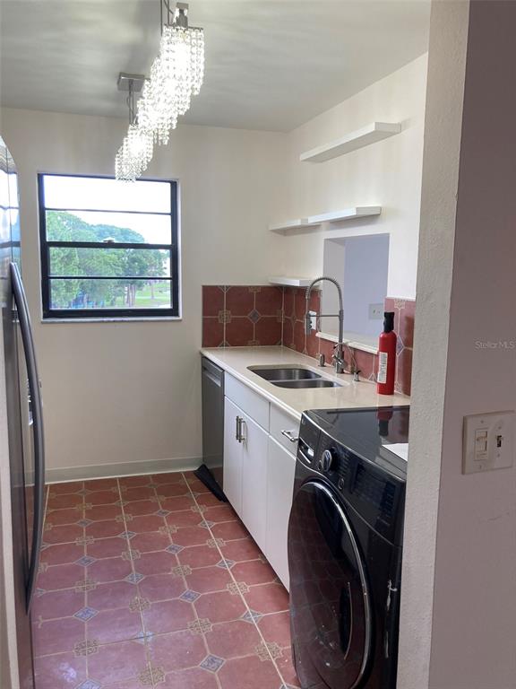 A kitchen features terracotta tile flooring, white cabinets, a black washer, and a crystal chandelier — 7975 58TH AVENUE N UNIT 408, ST PETERSBURG, FL