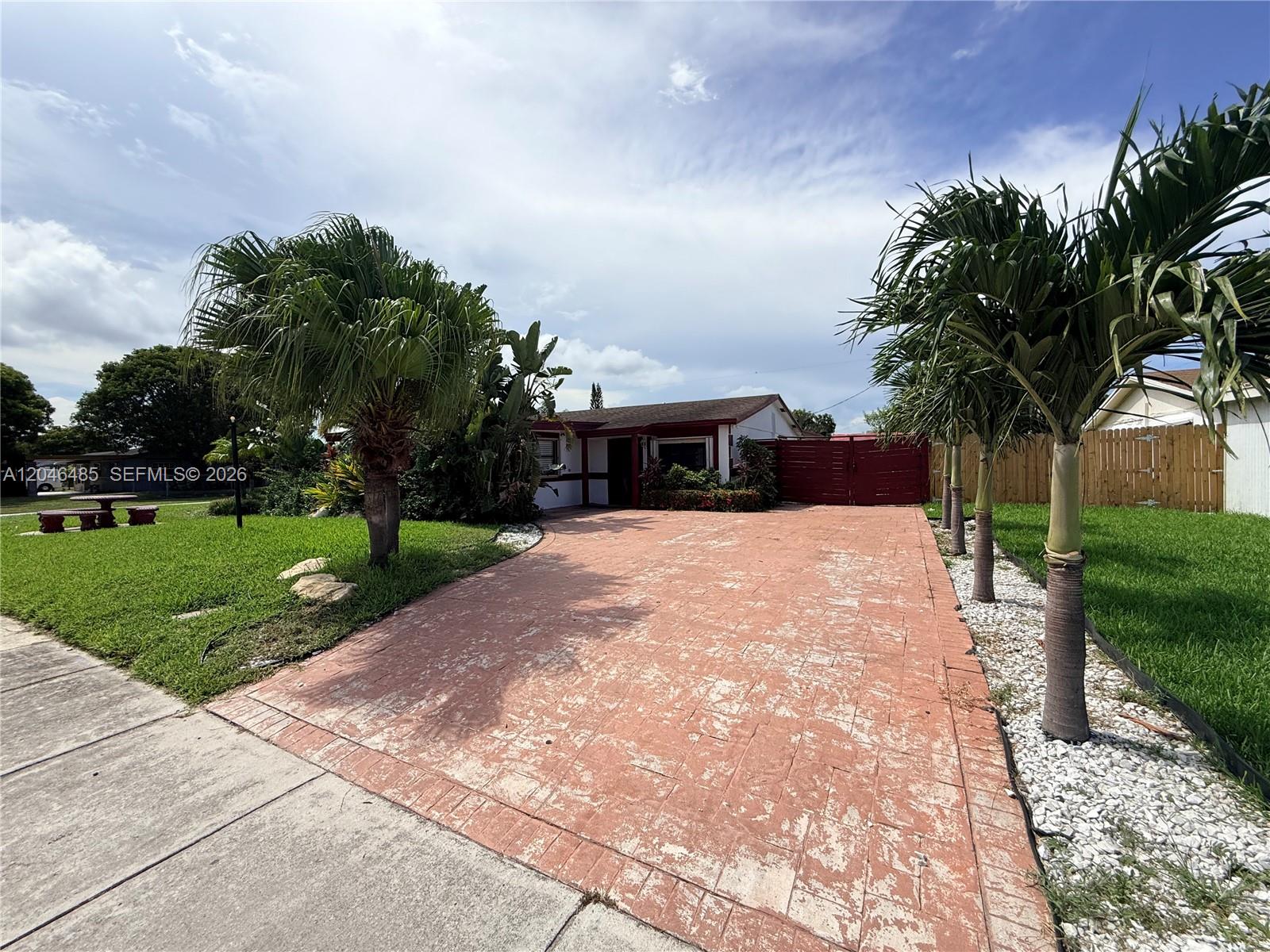 A single-story house features a stamped concrete driveway, palm trees, and a red gate — 323 NW 4th Pl, Deerfield Beach FL 33441, DEERFIELD BEACH, FL