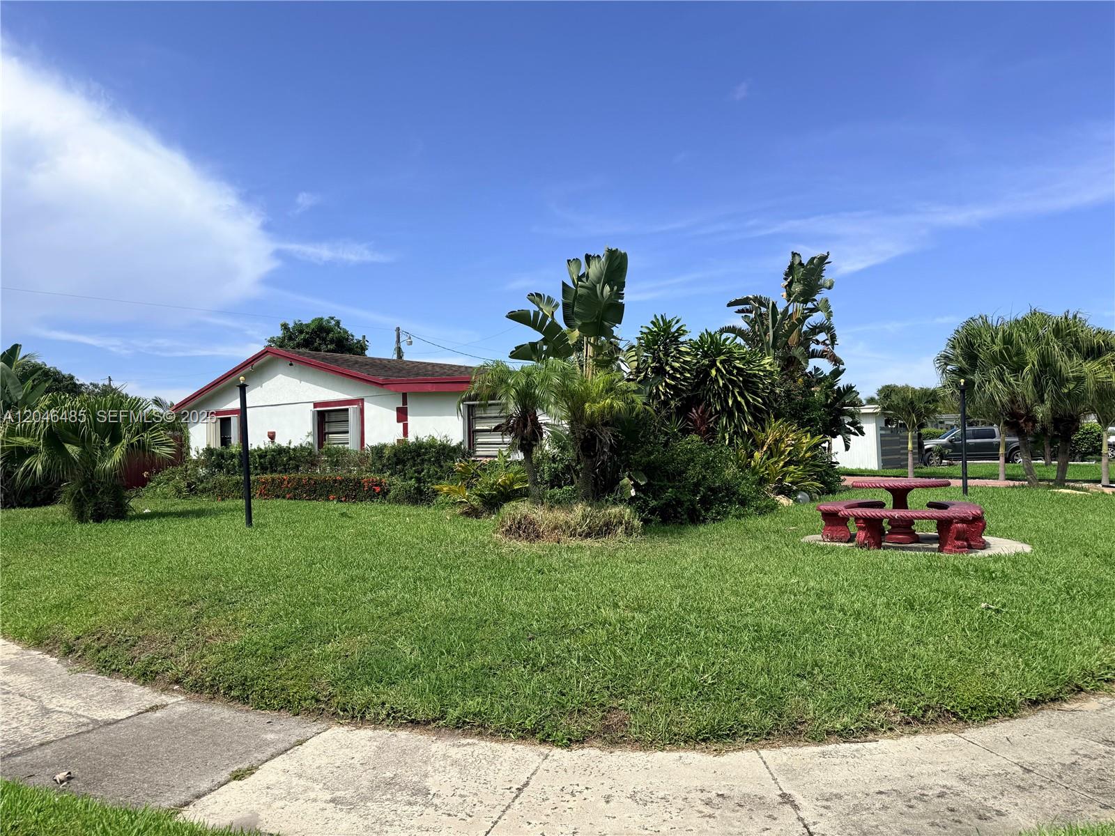 A white house with a red roof sits behind a lawn with tropical landscaping — 323 NW 4th Pl, Deerfield Beach FL 33441, DEERFIELD BEACH, FL