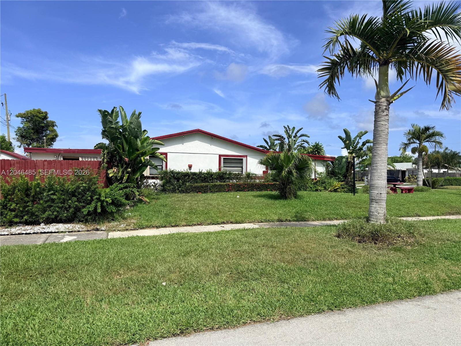 A single-story house with a white exterior and red trim sits behind a green lawn — 323 NW 4th Pl, Deerfield Beach FL 33441, DEERFIELD BEACH, FL