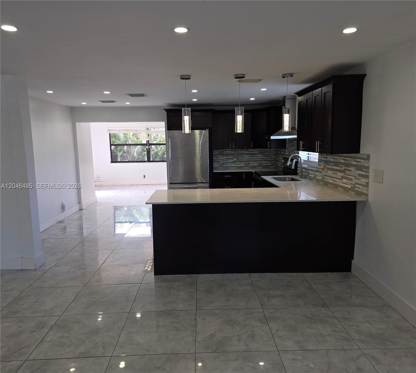 A kitchen with dark cabinets, stainless steel appliances, and a peninsula overlooks a tiled room — 323 NW 4th Pl, Deerfield Beach FL 33441, DEERFIELD BEACH, FL