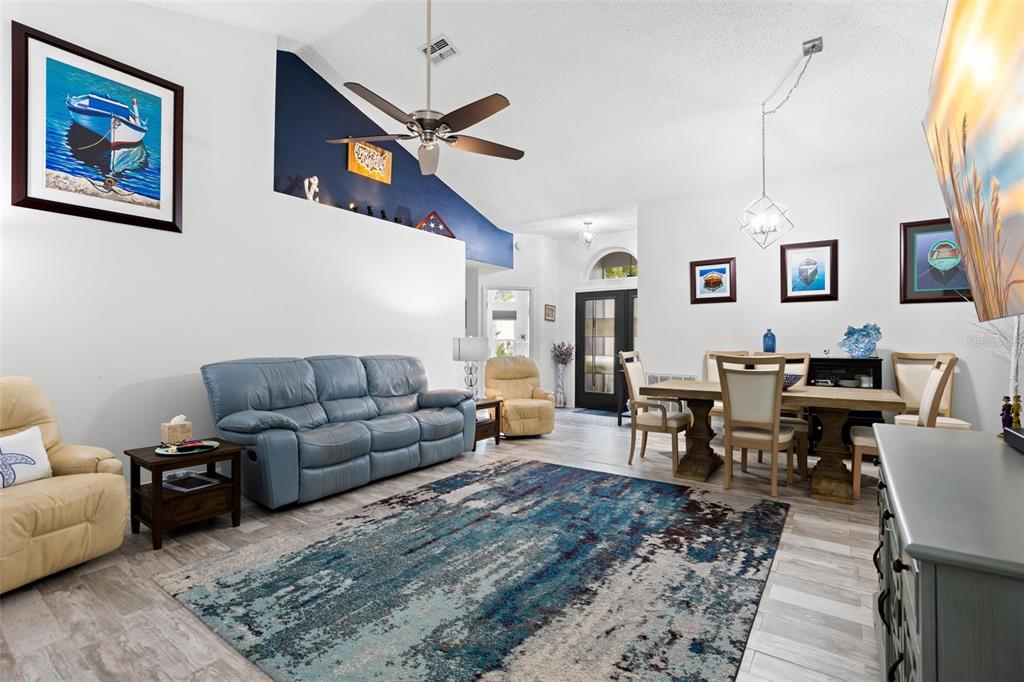 A living and dining area features a blue sofa, area rug, and vaulted ceilings — 1911 E DEL WEBB BOULEVARD, SUN CITY CENTER, FL