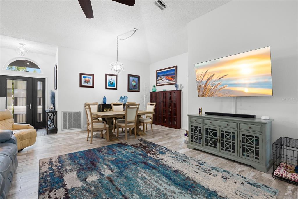 A living and dining area features light wood floors, a large area rug, and a television — 1911 E DEL WEBB BOULEVARD, SUN CITY CENTER, FL