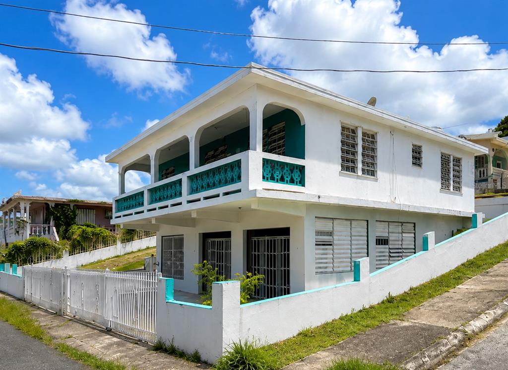 A two-story white house with a turquoise balcony railing and a gated front yard — 461 Comm. Mariani BO. EMAJAGUA, MAUNABO, PR