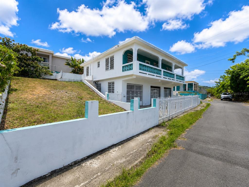 A two-story white house with a balcony and a fenced yard sits along a road — 461 Comm. Mariani BO. EMAJAGUA, MAUNABO, PR
