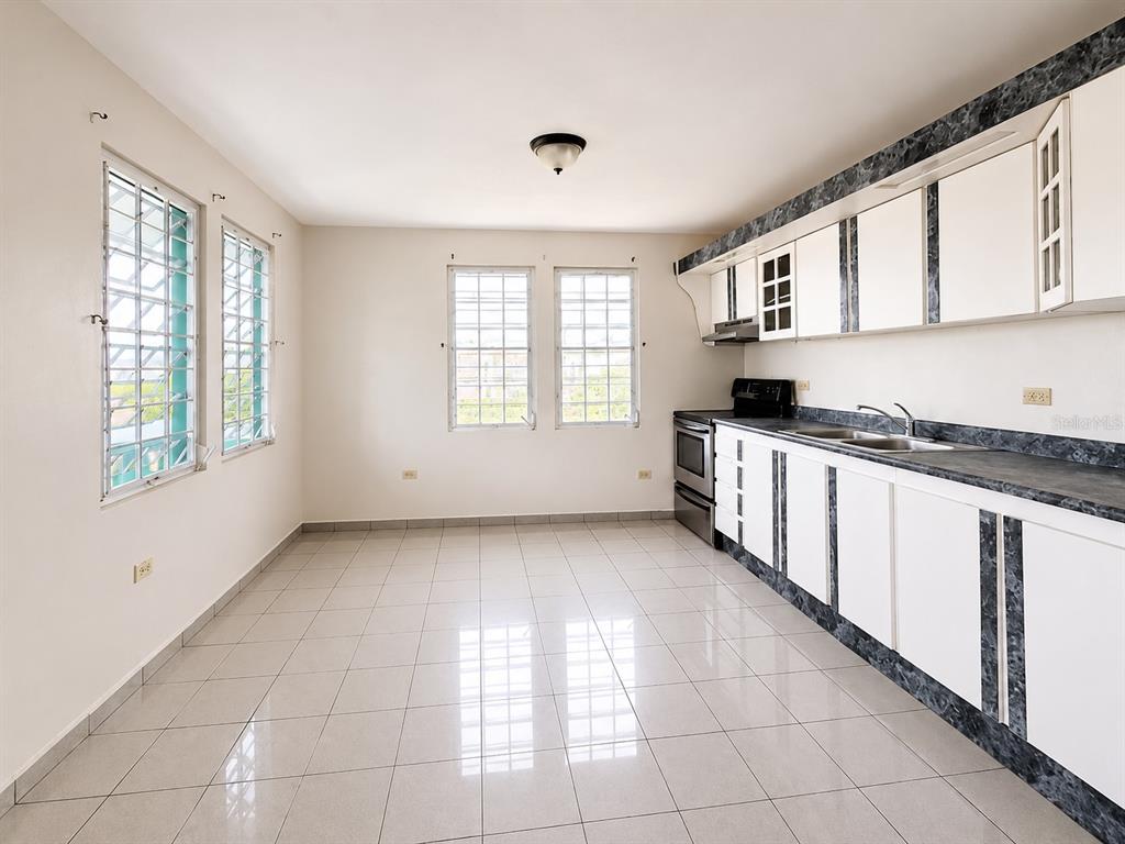 A kitchen with white cabinets, dark countertops, tiled floors, and multiple windows with security bars — 461 Comm. Mariani BO. EMAJAGUA, MAUNABO, PR