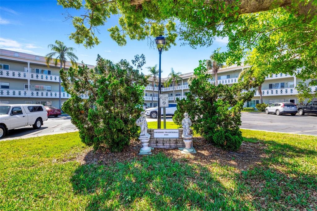 A lamp post and two statues stand in a landscaped island before a multi-story apartment building — 2401 ECUADORIAN WAY UNIT 57, CLEARWATER, FL