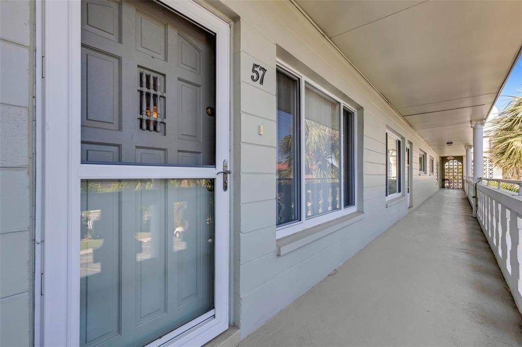 A gray exterior door with a storm door and a window on a covered walkway — 2401 ECUADORIAN WAY UNIT 57, CLEARWATER, FL