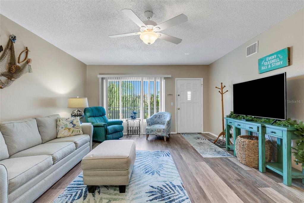 A living room features a sofa, teal recliner, television on a console, and a ceiling fan — 2401 ECUADORIAN WAY UNIT 57, CLEARWATER, FL