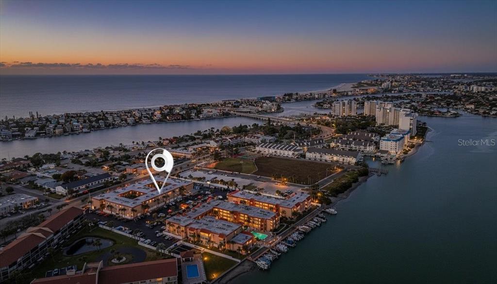 An aerial view shows a multi-story residential complex near a waterway and coastal beach — 8911 BLIND PASS ROAD UNIT 118, ST PETE BEACH, FL
