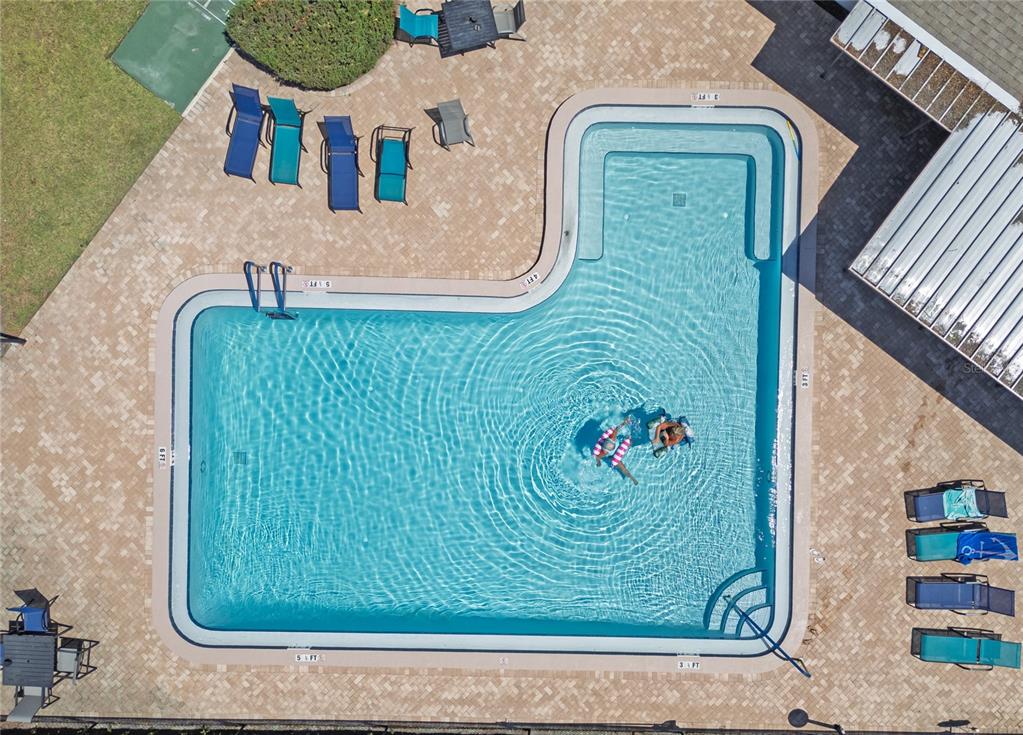 An aerial view shows an L-shaped swimming pool surrounded by a paved deck and lounge chairs — 2444 ENTERPRISE ROAD UNIT 29, CLEARWATER, FL
