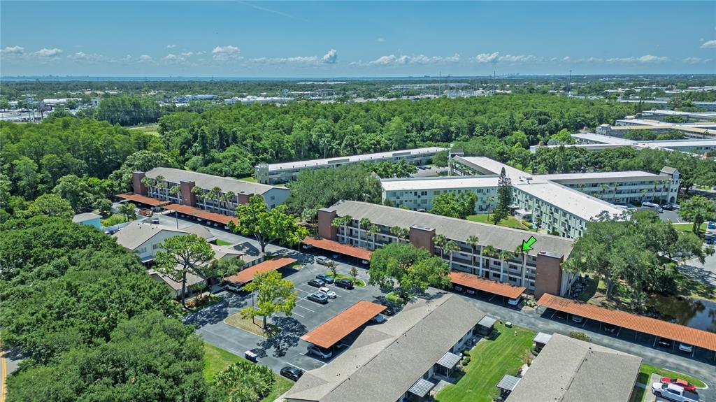 An aerial view shows multiple apartment buildings with covered parking lots and surrounding trees — 2444 ENTERPRISE ROAD UNIT 29, CLEARWATER, FL