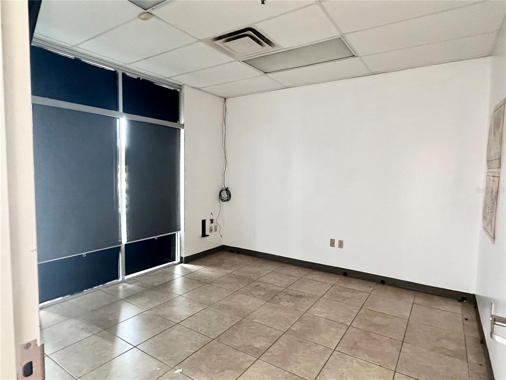 An empty office room features light-colored tile flooring, white walls, and a large window — 1700 35TH STREET UNIT 103, ORLANDO, FL