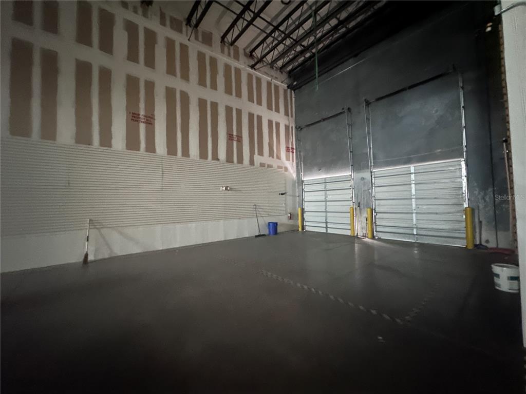 An empty warehouse space features high ceilings, concrete floors, and two large roll-up doors — 1700 35TH STREET UNIT 103, ORLANDO, FL