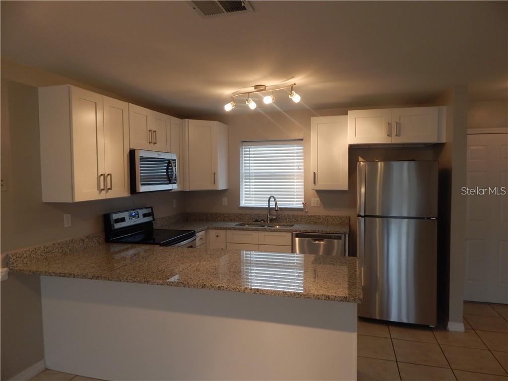 A kitchen features white cabinets, granite countertops, stainless steel appliances, and a breakfast bar — 307 SHERBORNE LANE, KISSIMMEE, FL