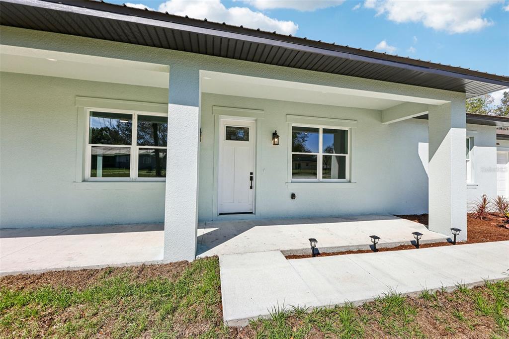 A light green house exterior features a covered front porch, white door, and concrete walkway — 1623 MAGNOLIA AVENUE, DELAND, FL