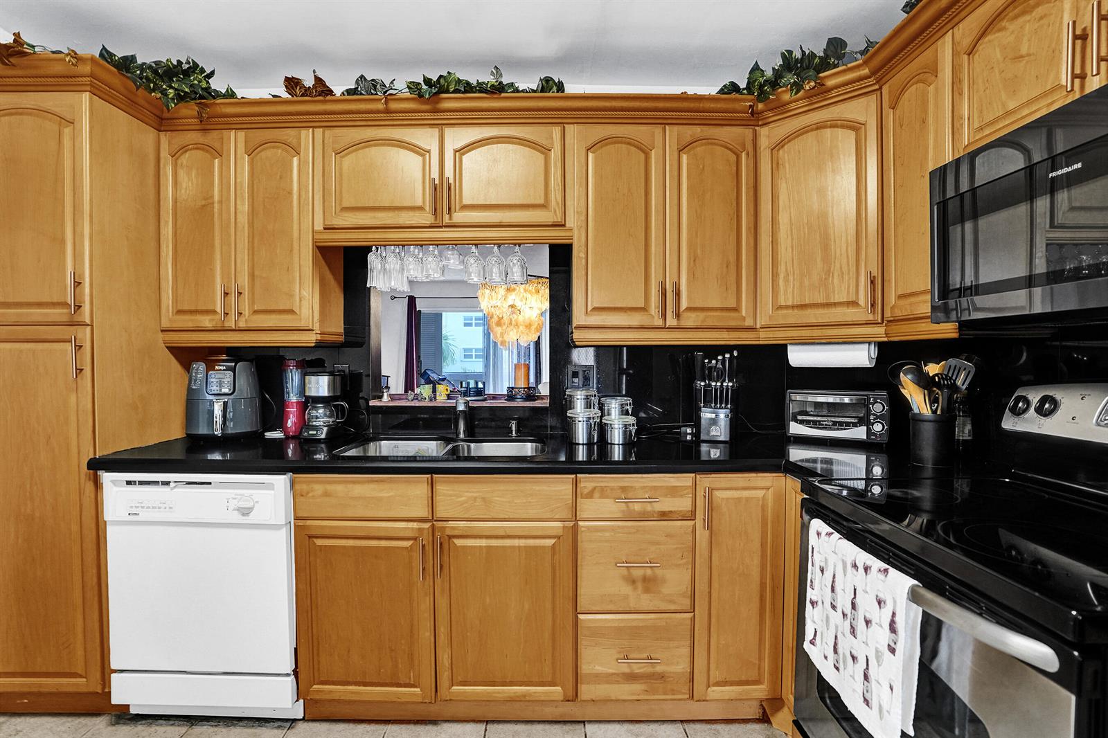 A kitchen with light wood cabinets, black countertops, a white dishwasher, and a black stove — 218 NE 12th Avenue # 401, Hallandale Beach FL 33009, HALLANDALE BEACH, FL