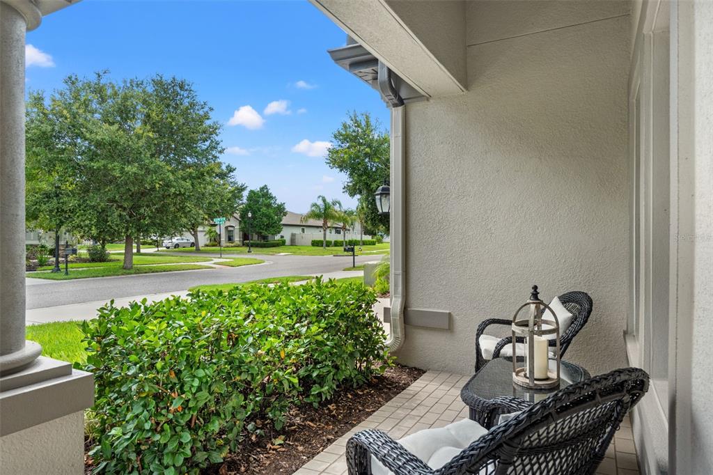 A covered front porch features wicker chairs, a small table, and a view of the street — 8320 BLUEVINE SKY DRIVE, LAND O LAKES, FL