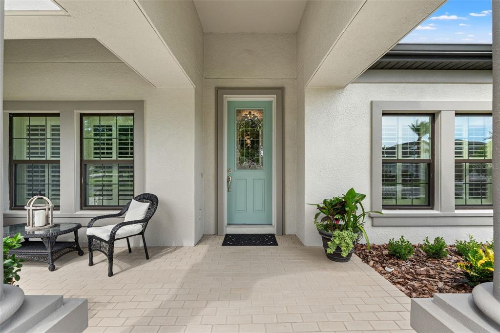 A covered front porch features a light blue door, a wicker chair, and potted plants — 8320 BLUEVINE SKY DRIVE, LAND O LAKES, FL