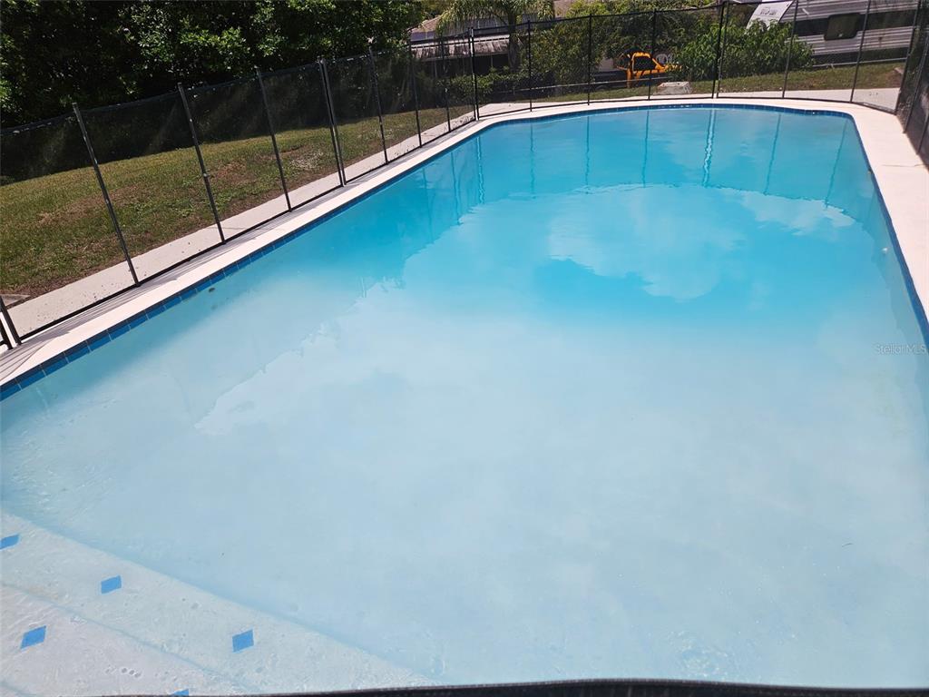 A rectangular swimming pool with a safety fence is surrounded by a concrete deck — 415 E BERESFORD AVENUE, DELAND, FL