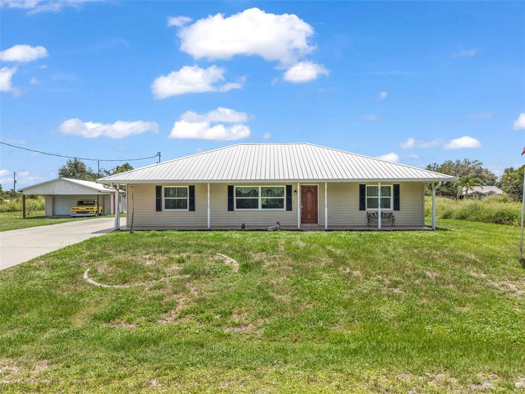 A single-story house with a metal roof and an attached carport sits on a lawn — 30 SUCCESS DRIVE, PUNTA GORDA, FL