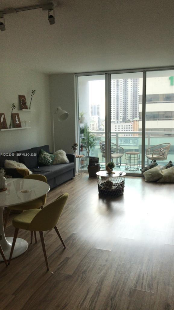 A living room with wood-look flooring, a gray sofa, and a balcony overlooking city buildings — 951 Brickell Ave # 1503, Miami FL 33131, MIAMI, FL