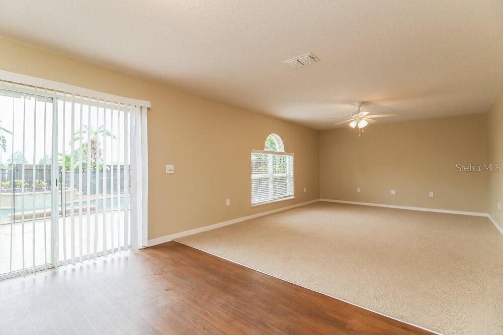 A living room with beige carpet, tan walls, a ceiling fan, and sliding glass doors — 13513 MANGO BAY DRIVE, RIVERVIEW, FL