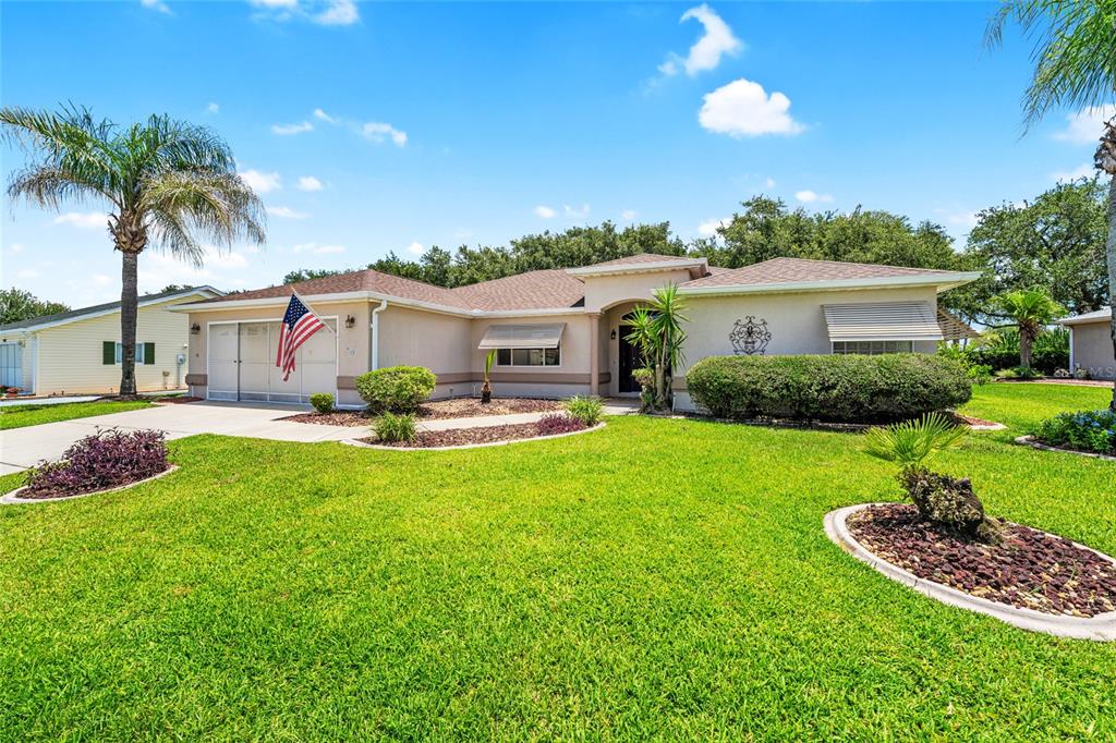 A single-story house with a tan exterior, a two-car garage, and a manicured front lawn — 9082 SE 135TH LOOP, SUMMERFIELD, FL