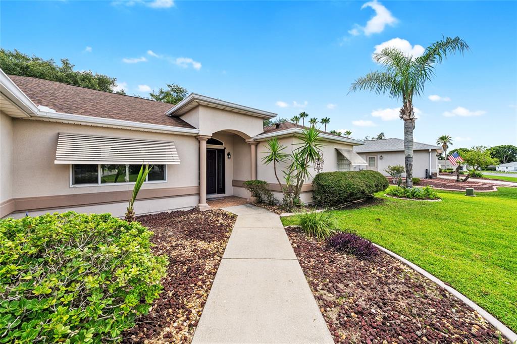 A single-story house with a beige stucco exterior, brown shingle roof, and a concrete walkway — 9082 SE 135TH LOOP, SUMMERFIELD, FL