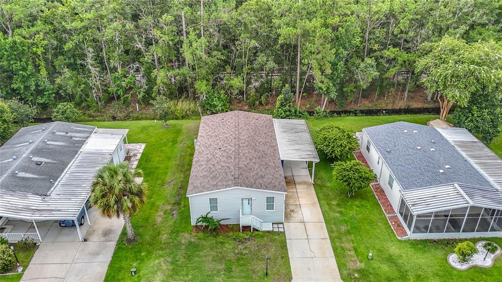 An aerial view shows three single-story houses with driveways and carports situated near a wooded area — 2908 KINGSWOOD CIRCLE, BROOKSVILLE, FL