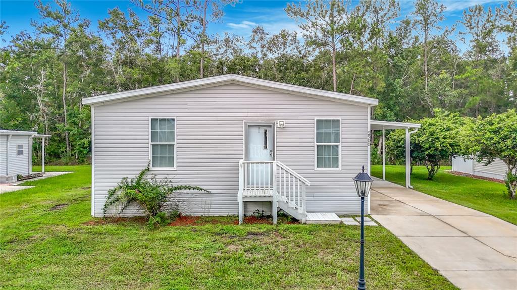 A single-story light gray vinyl-sided house features a front porch, driveway, and surrounding lawn — 2908 KINGSWOOD CIRCLE, BROOKSVILLE, FL