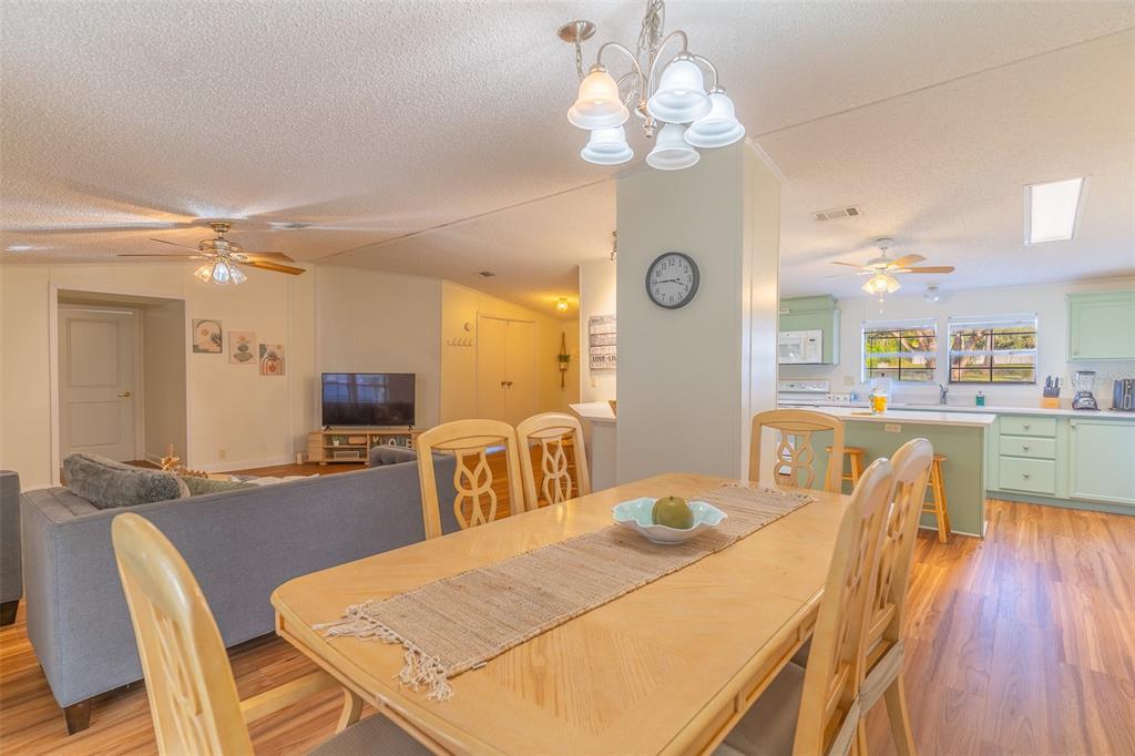 An open-concept living and dining area features light wood flooring, a central kitchen, and furniture — 5028 CLEWIS AVENUE, TAMPA, FL