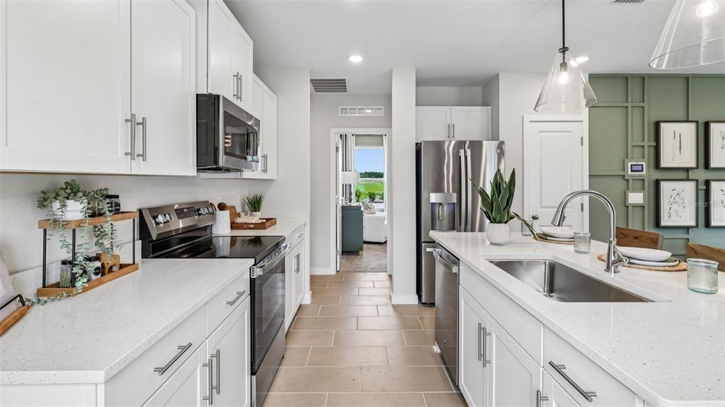 A modern kitchen features white cabinets, stainless steel appliances, a quartz island, and tile flooring — 428 LIBERTY BEND, HAINES CITY, FL