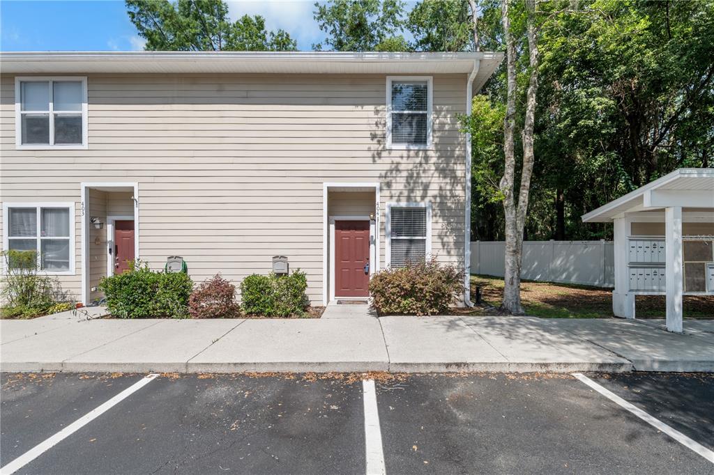 A two-story tan townhouse exterior features a sidewalk, parking spaces, and a mailbox kiosk — 1710 NW 7TH STREET UNIT 404, GAINESVILLE, FL